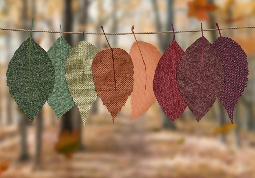 Fabric leaves hang on a rope, showcasing autumn colors in a forest backdrop.